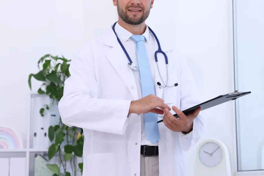 medical consultant in a white coat and stethoscope reviewing patient information on a clipboard in a bright clinic.