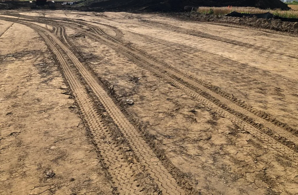 Subgrade rutting and tire deflection on clay soil indicating failed proof-roll before base installation.