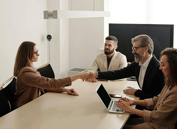 A woman sitting at a desk in a bright office, working on a laptop with notebooks, a cup, and a desk lamp beside her.