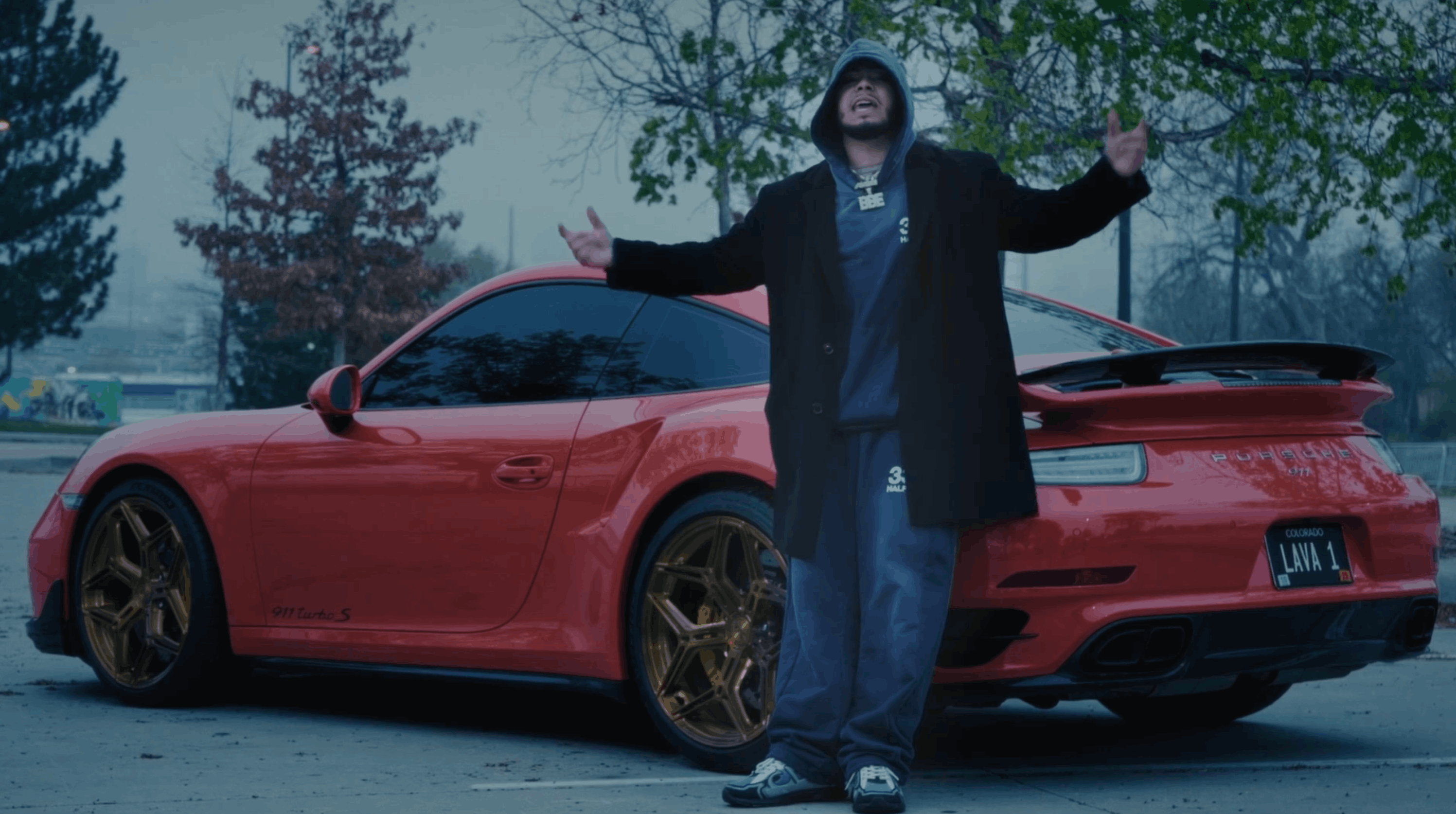 Griselda Rapper E Murda standing in front of a red sports car in a cinematic music video scene
