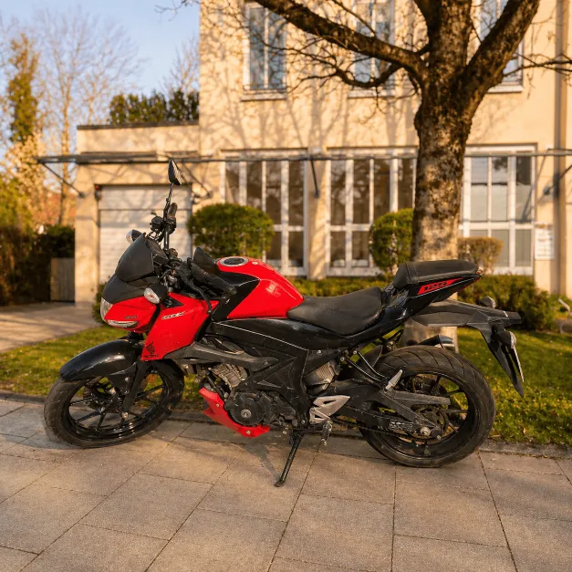 Ein sportliches, rot-schwarzes Motorrad parkt auf einem Gehweg vor dem Fahrschulgebäude im Sonnenlicht.