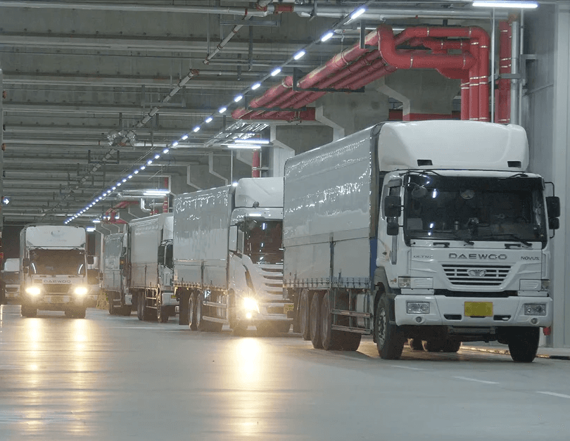 씨제이대한통운 더 운반 운송 차량들이 전국 인프라를 기반으로 물류센터 내부를 줄지어 이동하고 있습니다.