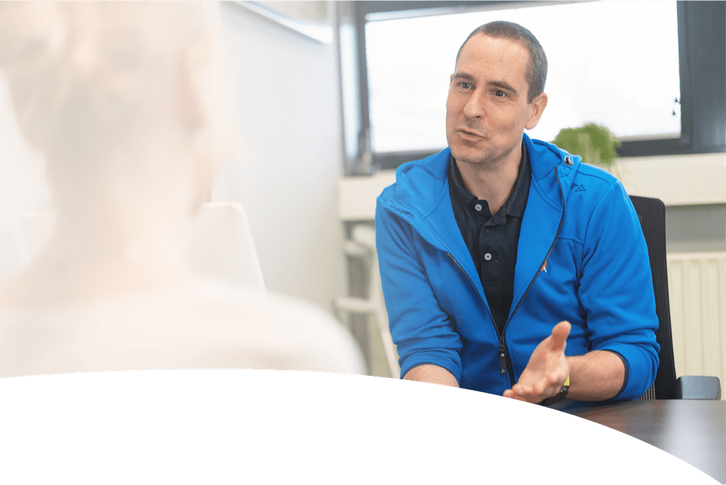 A group of four people, two men and two women, stand together smiling in a bright, modern office hallway, dressed in casual professional attire.