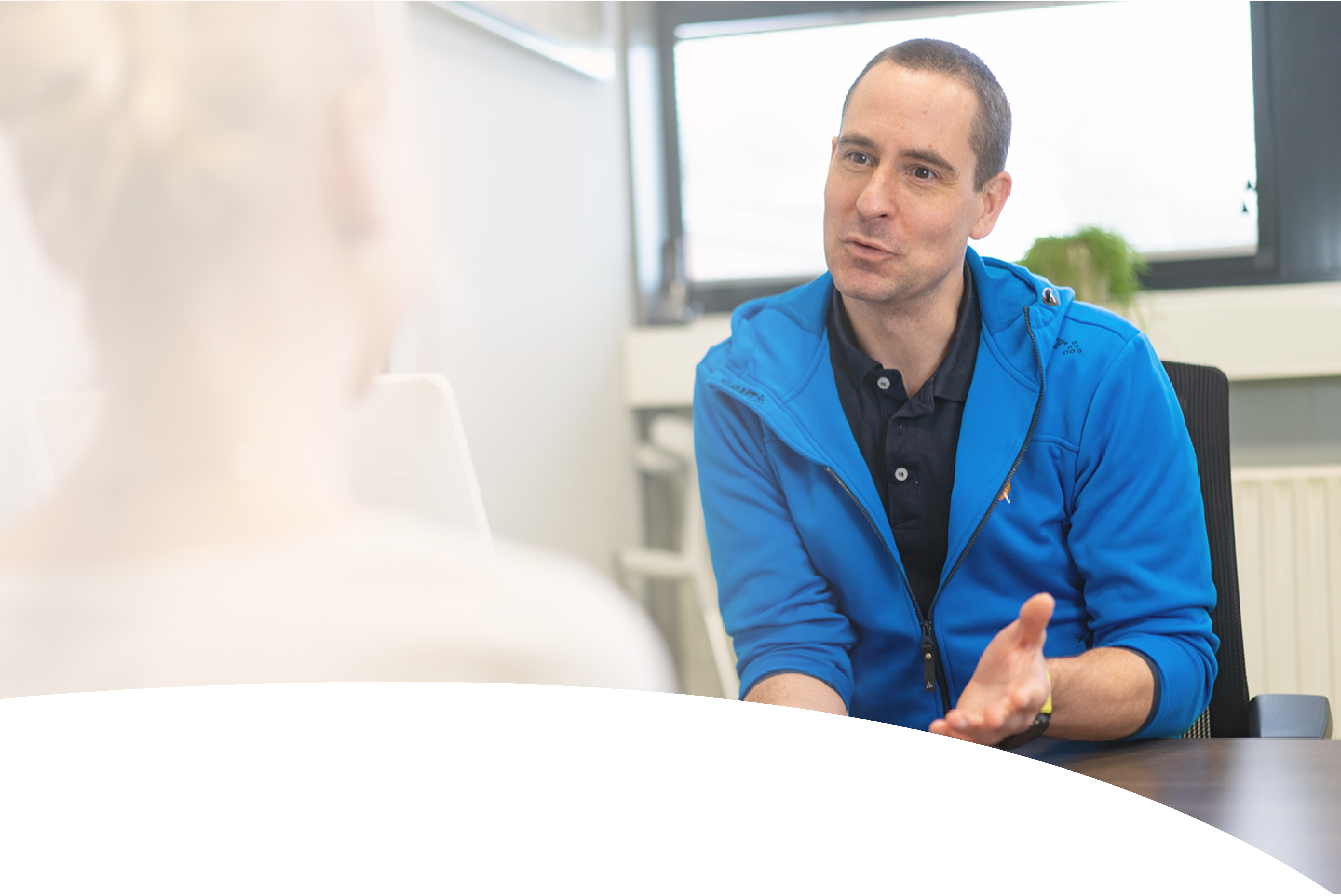 A group of four people, two men and two women, stand together smiling in a bright, modern office hallway, dressed in casual professional attire.