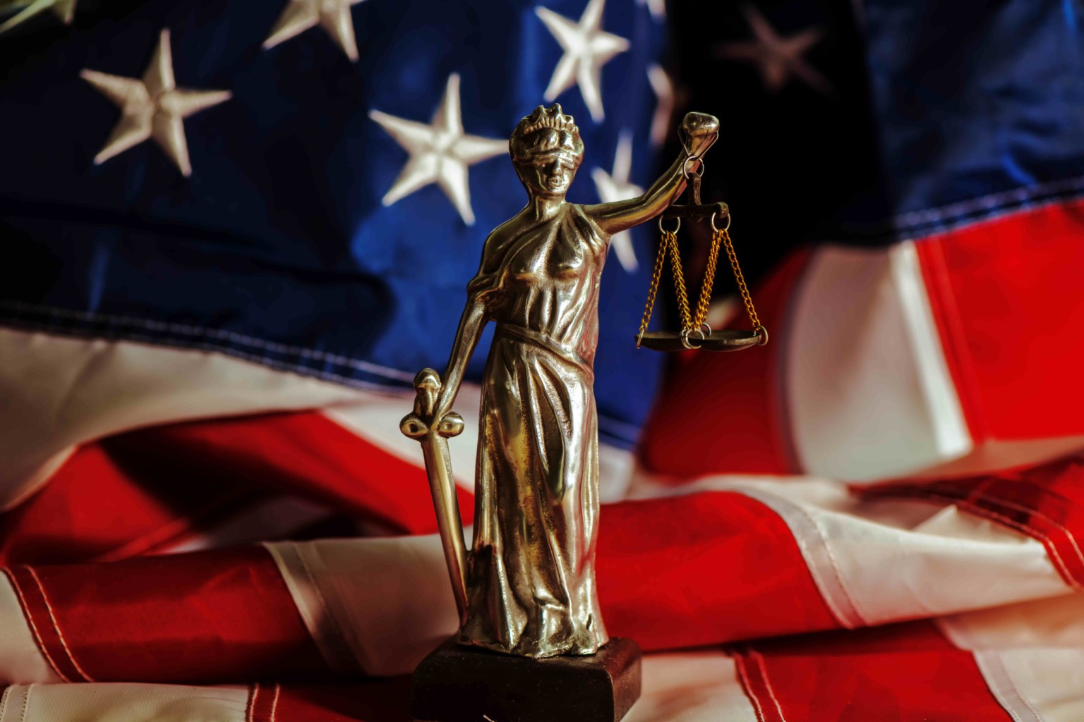 Lady justice statue standing before the American flag.