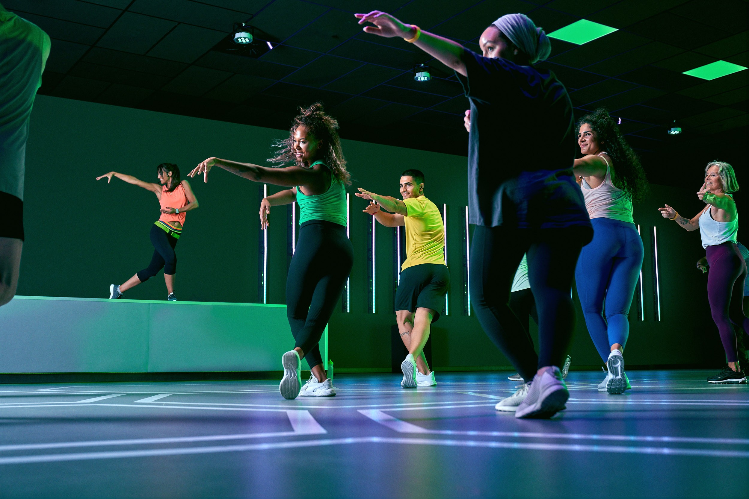 Dynamische Gruppe beim Zumba in einem XTRAFIT Studio mit energiegeladener Atmosphäre und grüner Beleuchtung unter Anleitung einer ausgebildeten Trainerin für Zumba.