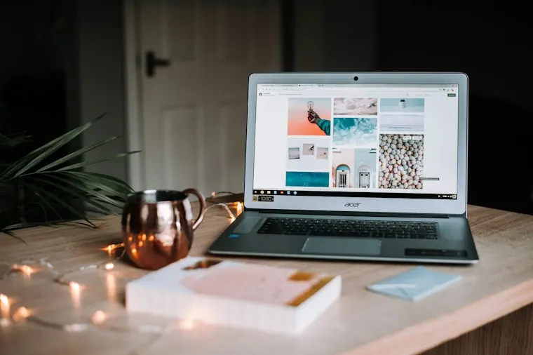 Laptop displaying a website beside a coffee cup on a wooden table.
