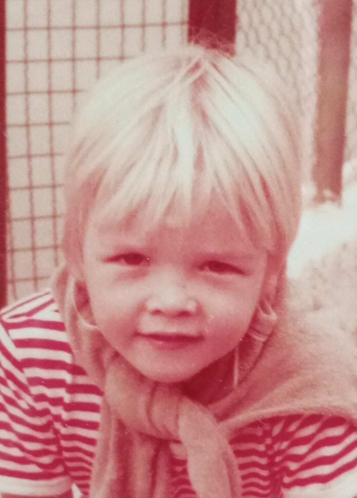 niño rubio con una camisa de rayas y un abrigo atado al cuello