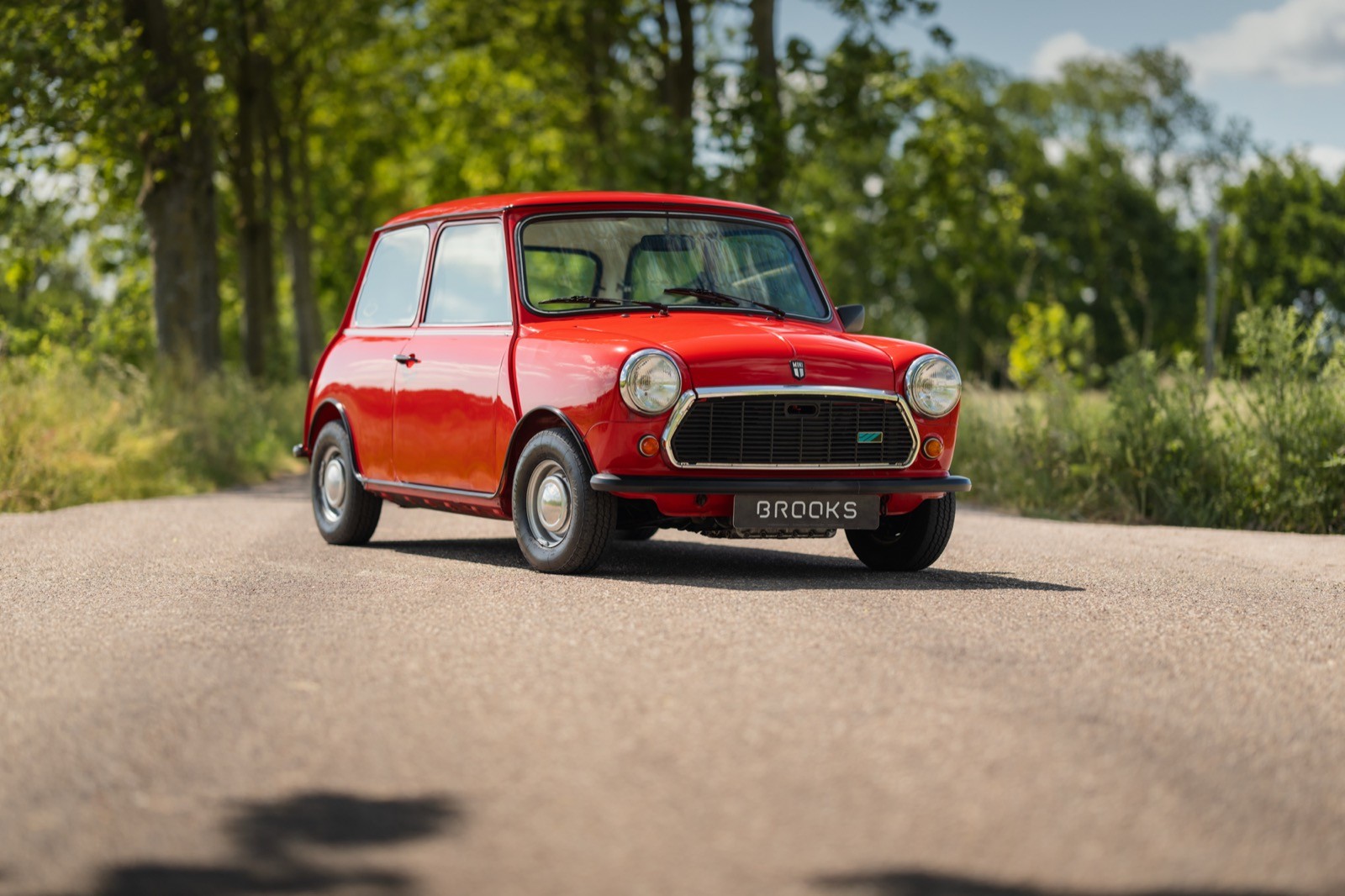 A classic red mini classic car with white details parked on a scenic road surrounded by greenery and trees.