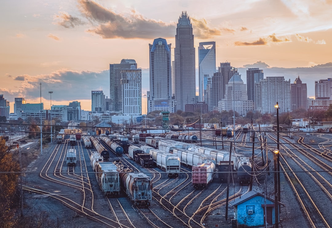Railroad yard with freight cars in the foreground and a city skyline at sunset.