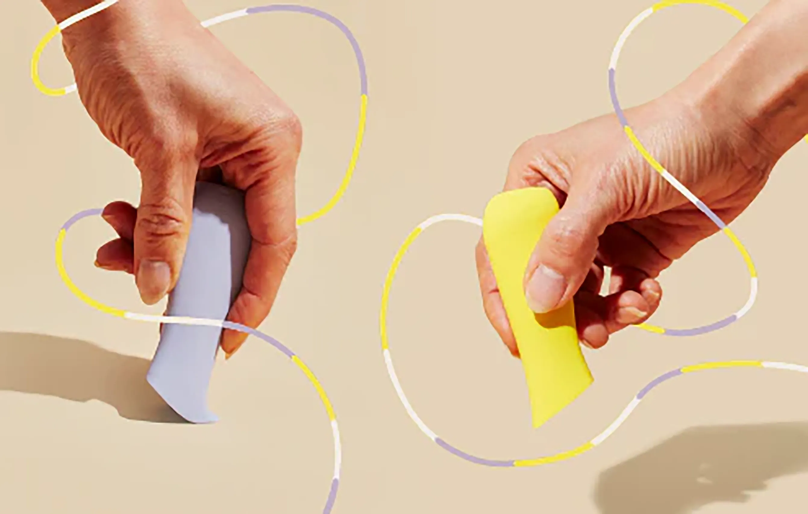 Hands holding gray and yellow Dame sexual wellness devices with looping graphic lines