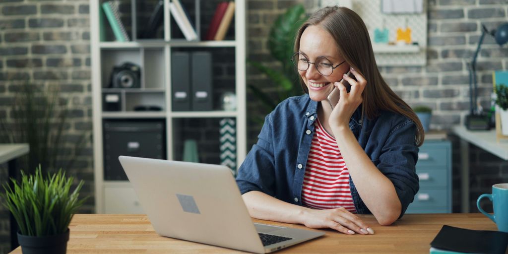 a woman talking on a cell phone while using a laptop