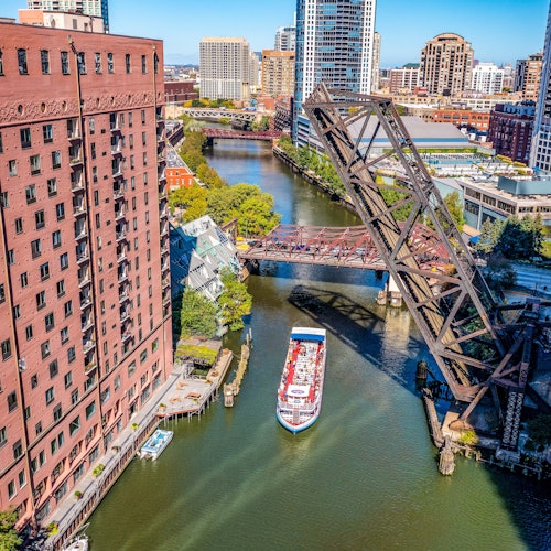 俯瞰一条贯穿城市的河流，河上有一艘船，周围是红色建筑，还有一座升起的铁桥。