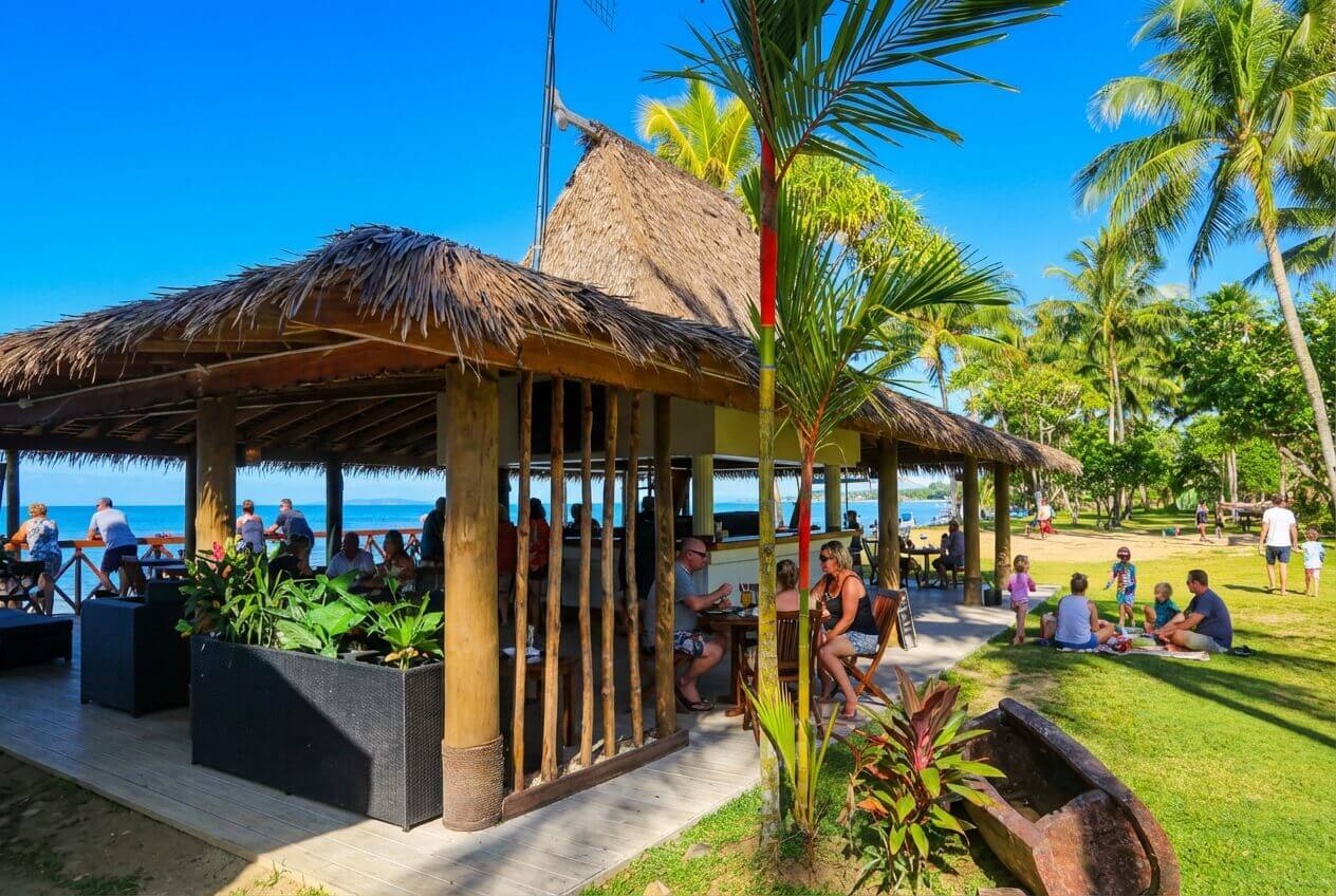 2 couples enjoying lunch at the beach front bar at Uprising Resort, Fiji served by a female staff member