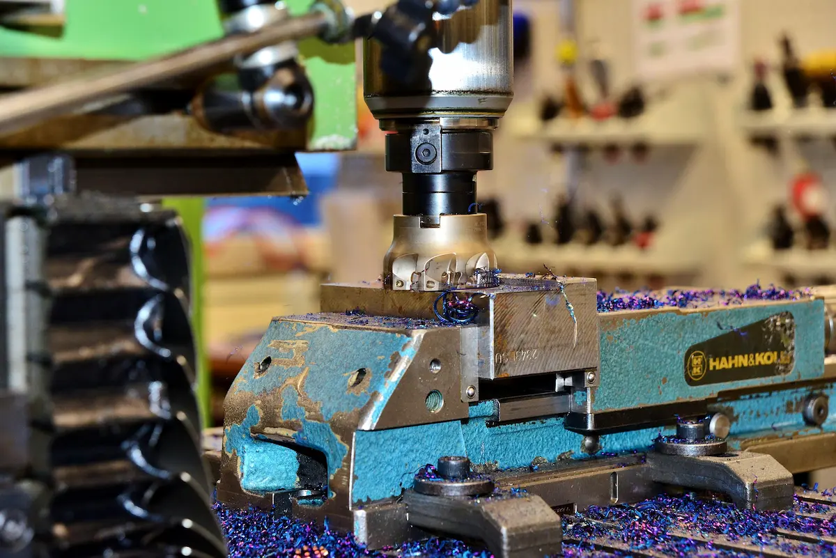 Close-up of a CNC milling machine cutting metal while blue metal chips scatter around the workpiece.