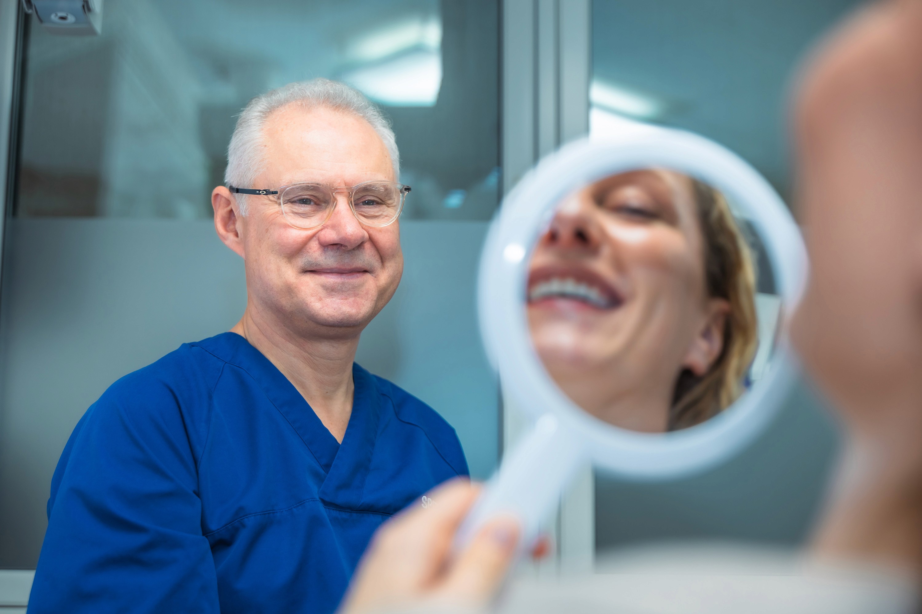 Fornøyd pasient ser behandlingsresultat i håndspeil sammen med tannlege Henrik Skjerven