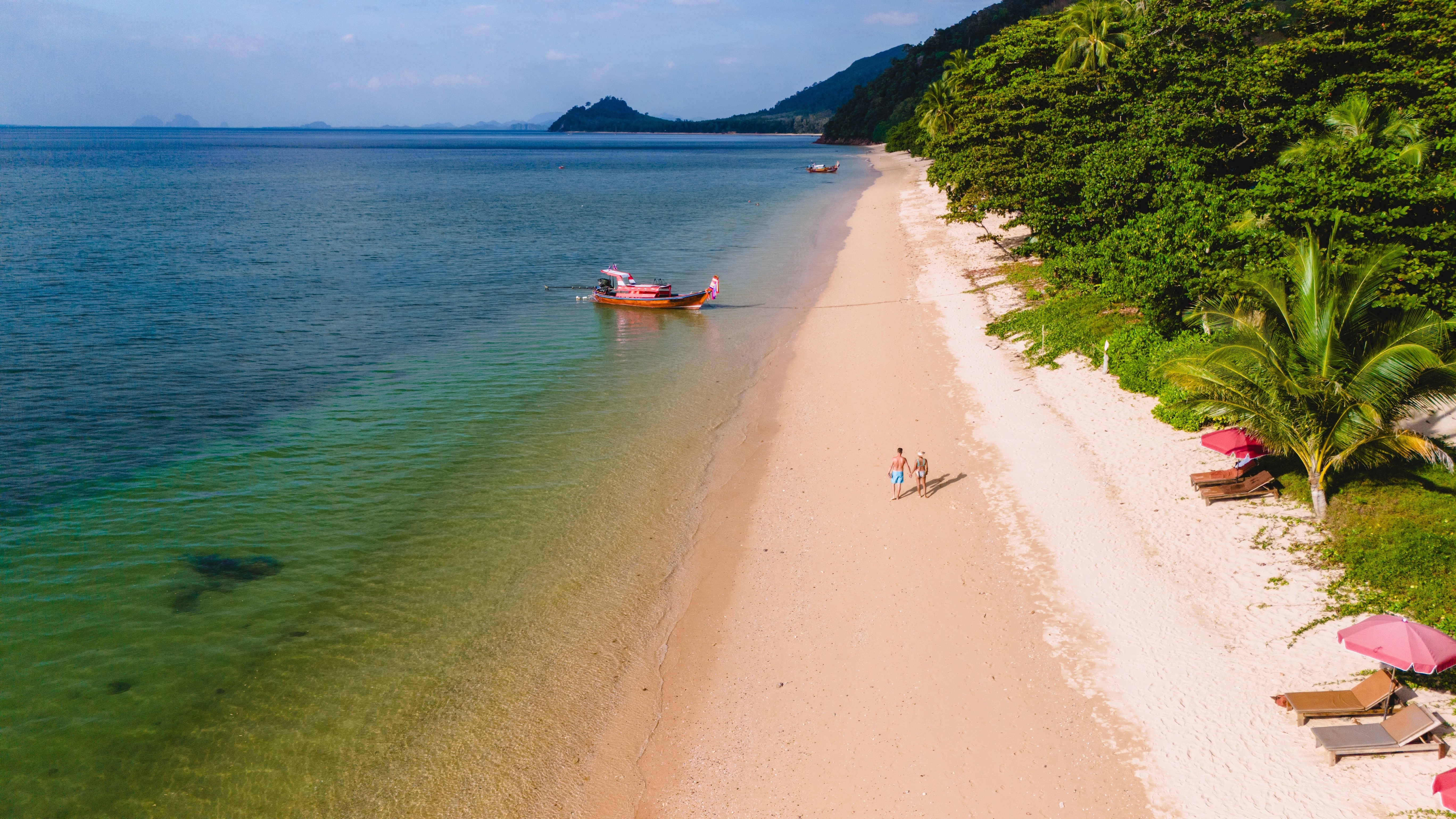 Two people walking along an empty beach with jungle on one side and the turquoise sea on the other, on Koh Libong, Thailand