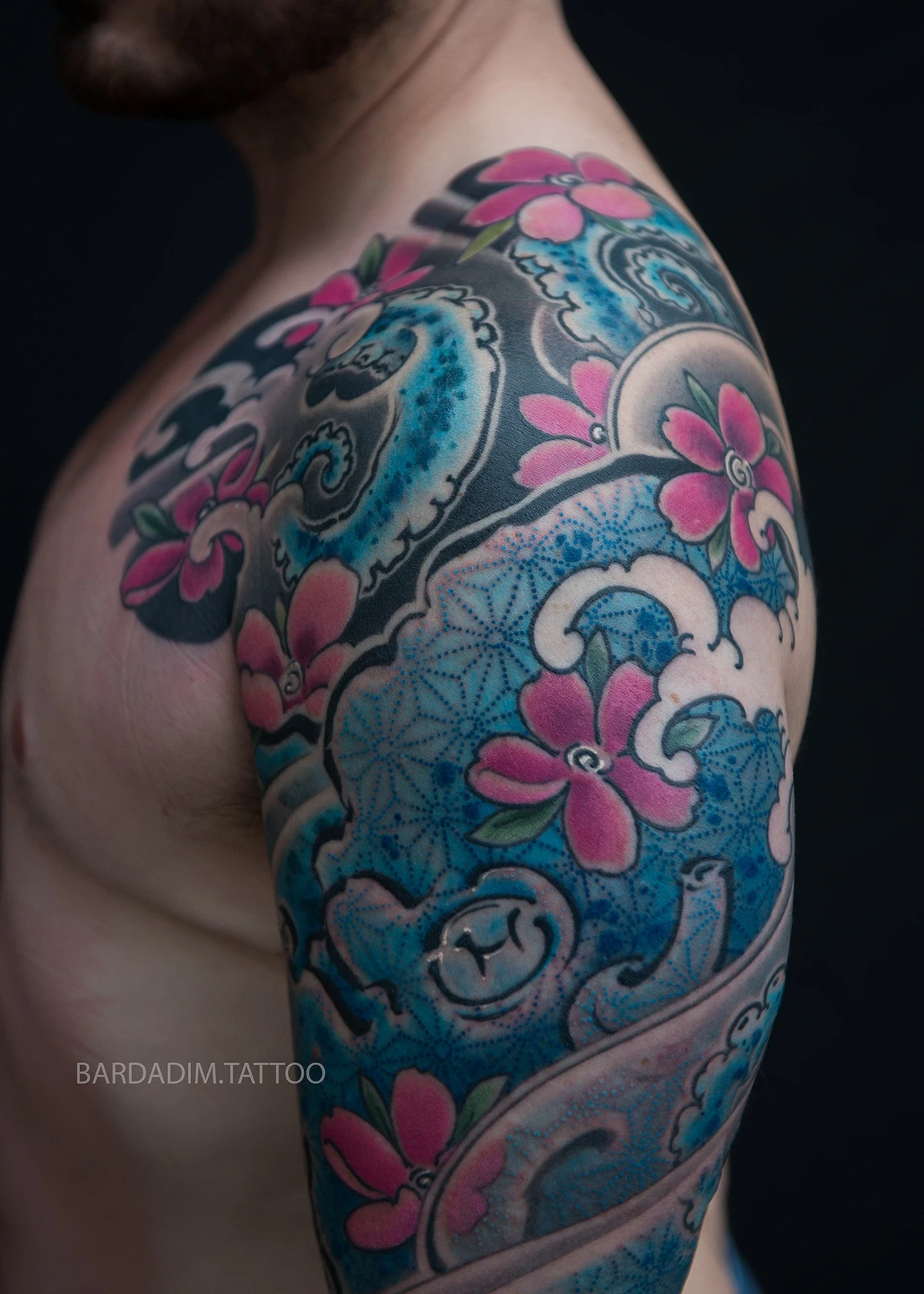 Close view of the upper arm: the asanoha hemp-leaf grid in dotwork across the blue skin of the octopus, its eye below and pink sakura around it.