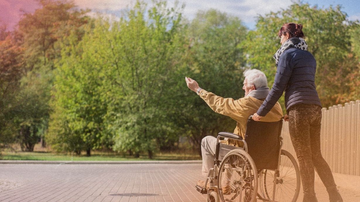 A caregiver, dressed in a black jacket and patterned scarf, assists a happy elderly gentleman in a wheelchair, pointing towards a lush green park, symbolizing active and engaging elder care with a focus on outdoor activities and nature exploration