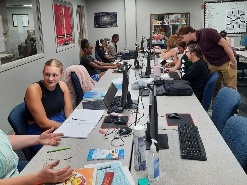 EXCEL students collaborating and working on computers along two long tables.