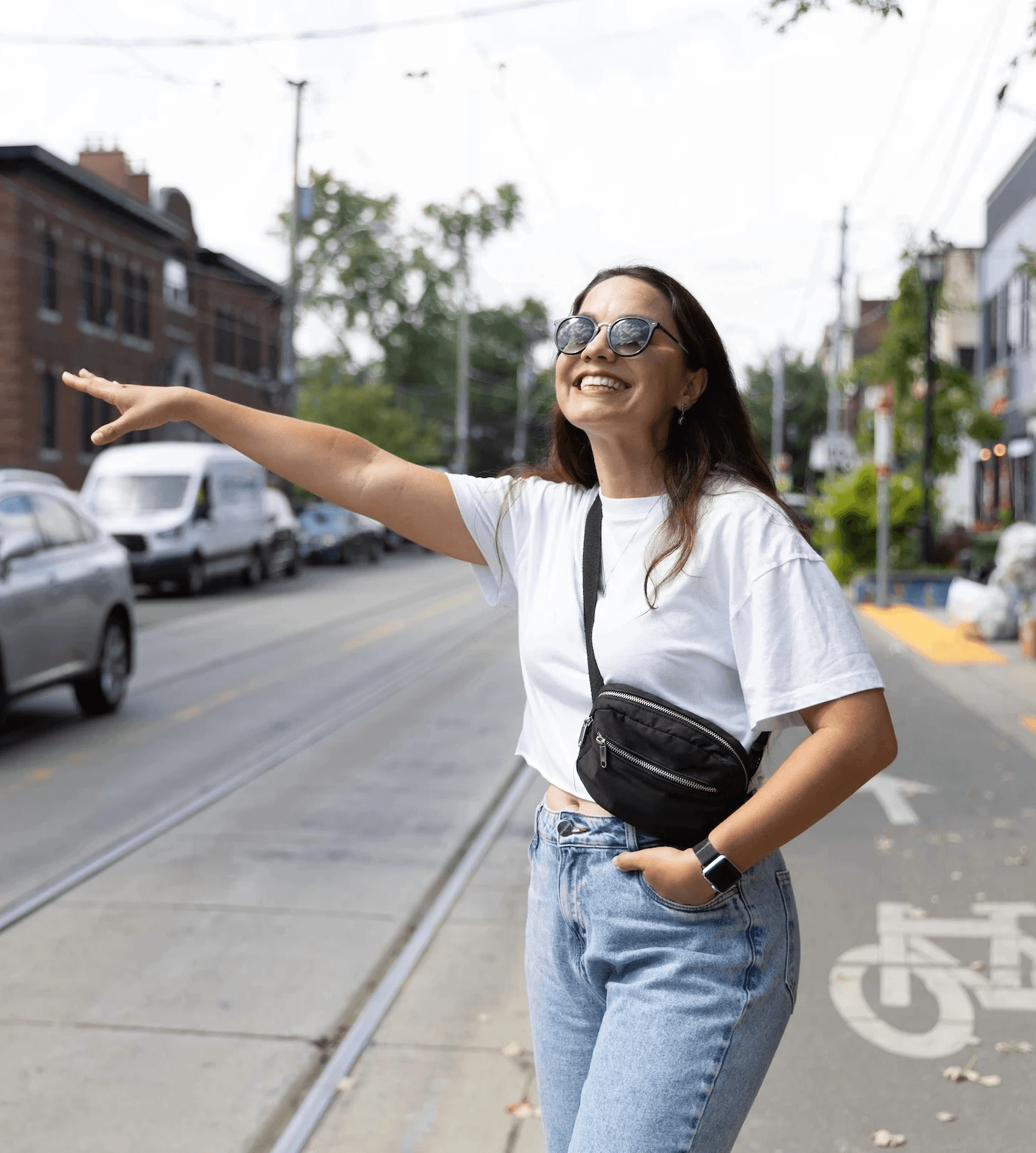 Mulher acenando para um carro em rua de Toronto, com expressão animada e óculos escuros.