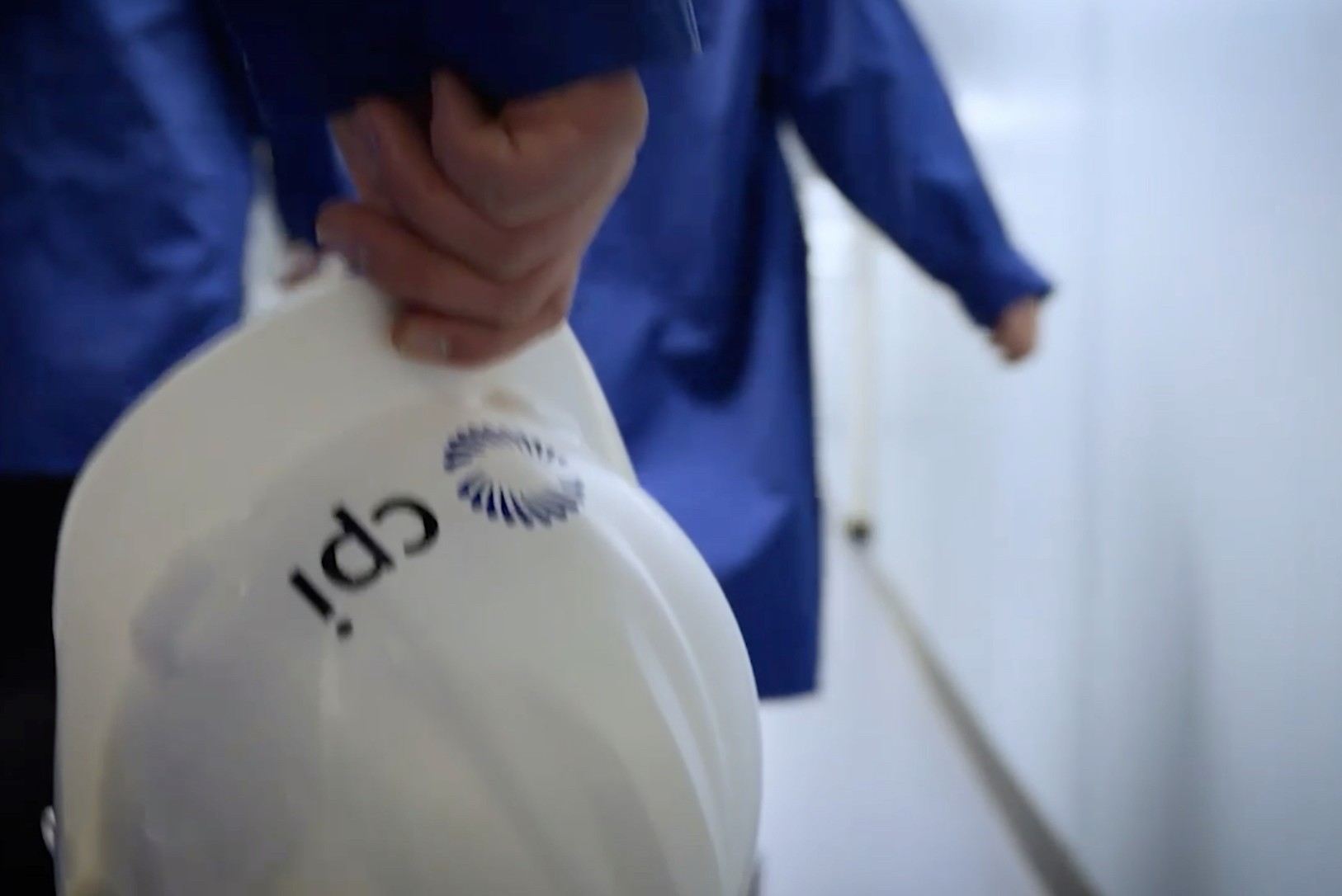 Person in a blue coat carrying a white hard hat printed with the CPI logo.