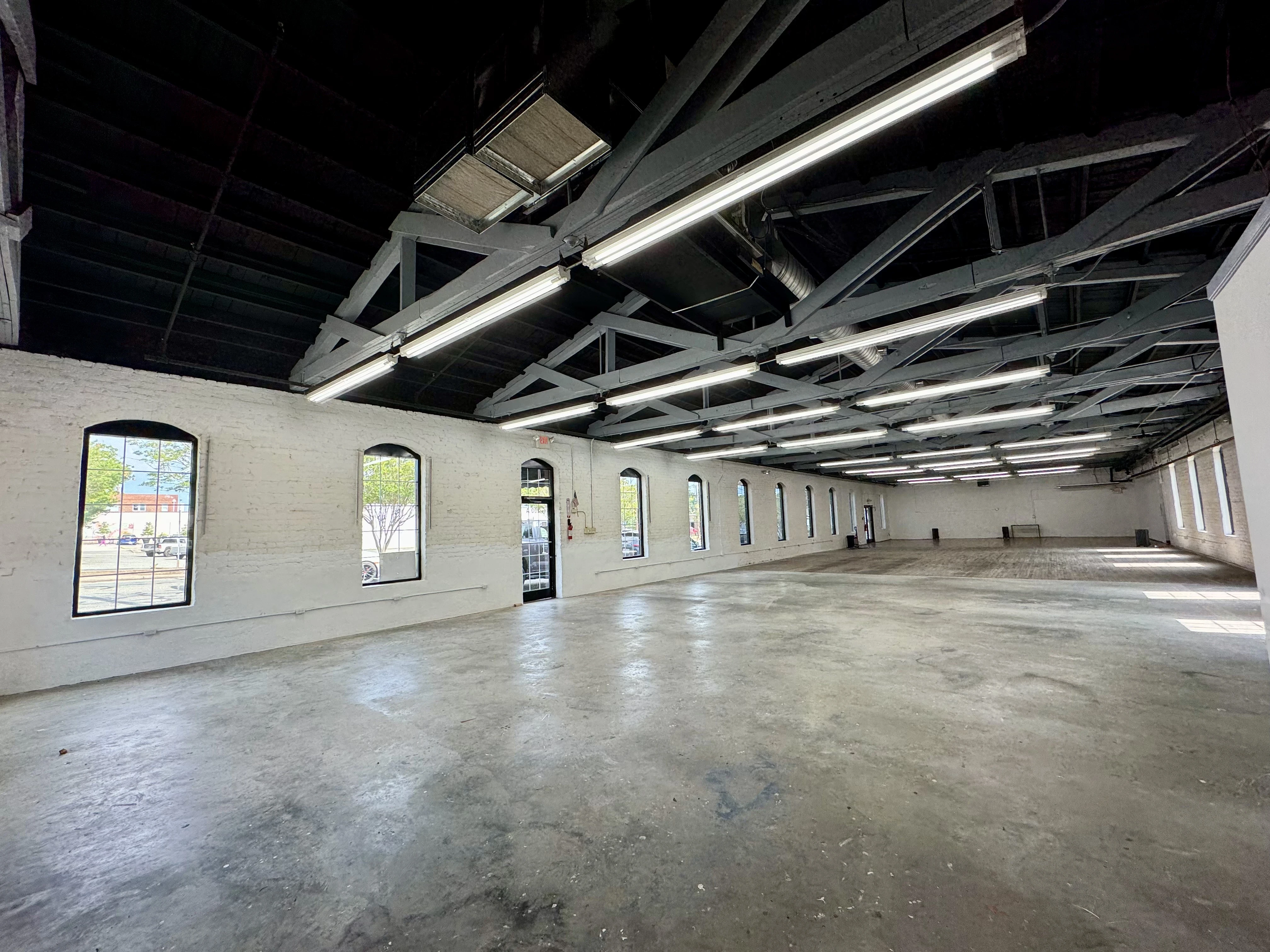 Open commercial interior with exposed ceiling beams, tall windows, and white brick walls