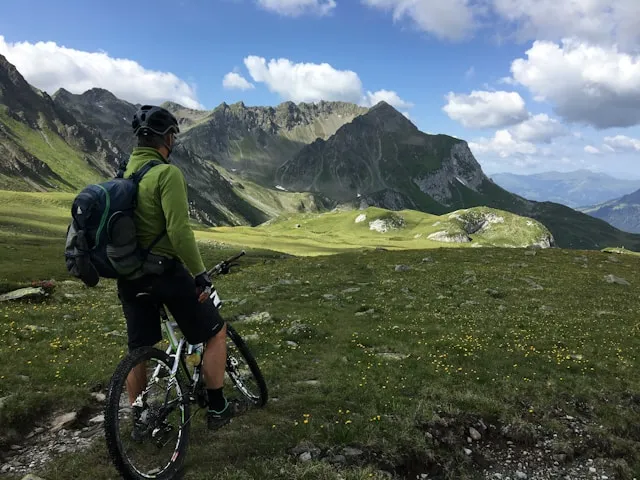 Mountain biker standing on an alpine trail above a green valley