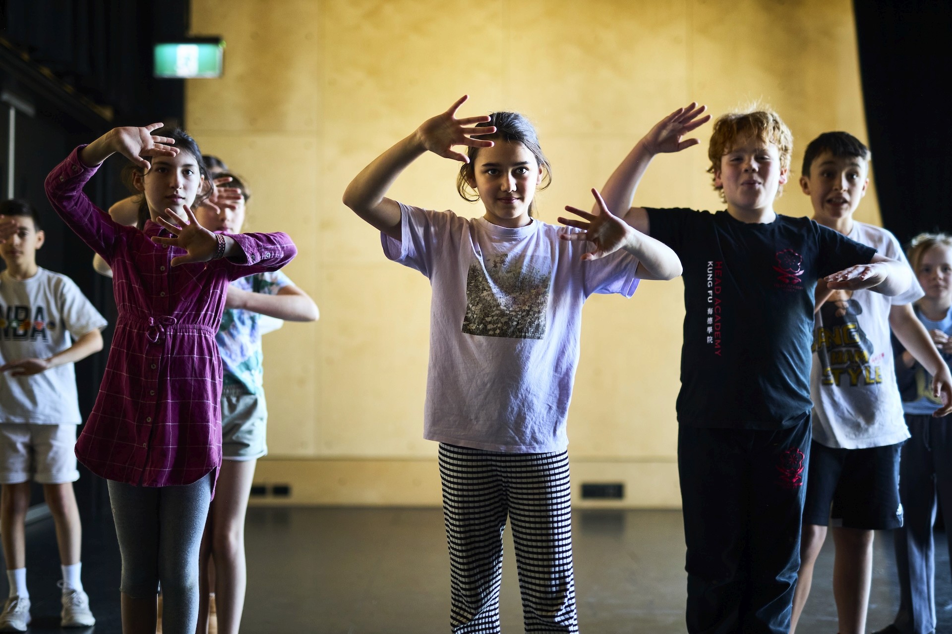 A group of young performers stand in formation, raising their hands in a coordinated movement exercise.