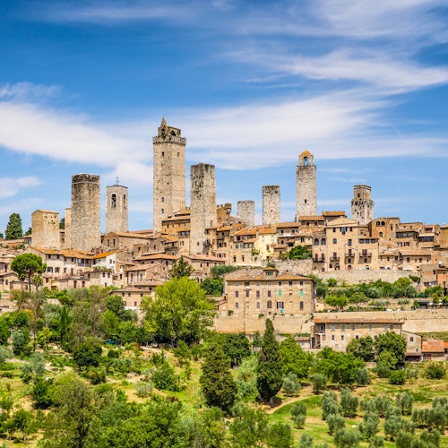 这座历史悠久的小镇拥有众多高耸的石塔，四周环绕着郁郁葱葱的绿色植物，蓝天下点缀着零星的白云。