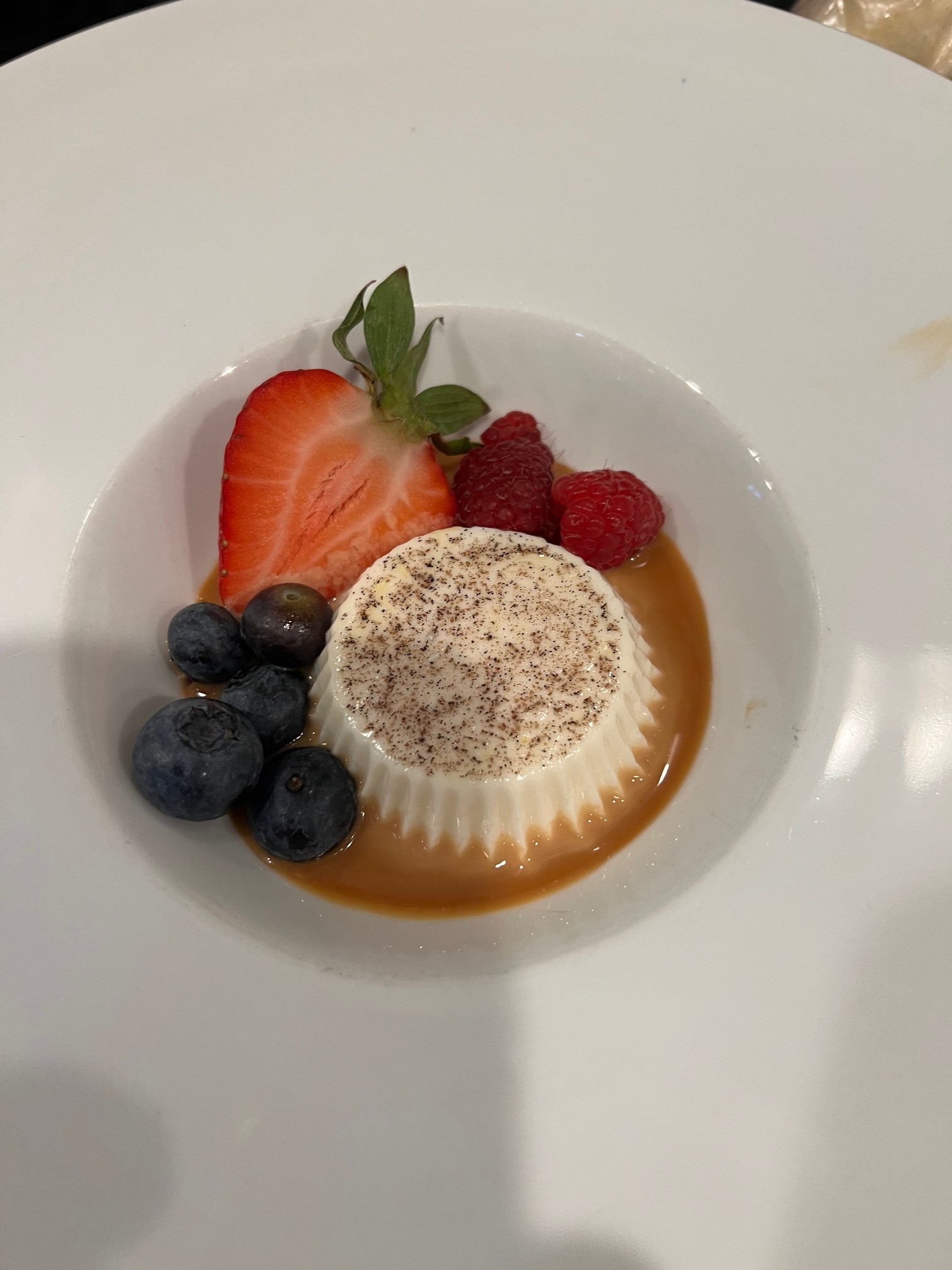 Panna cotta dessert with strawberry, raspberries, and blueberries on a white plate.