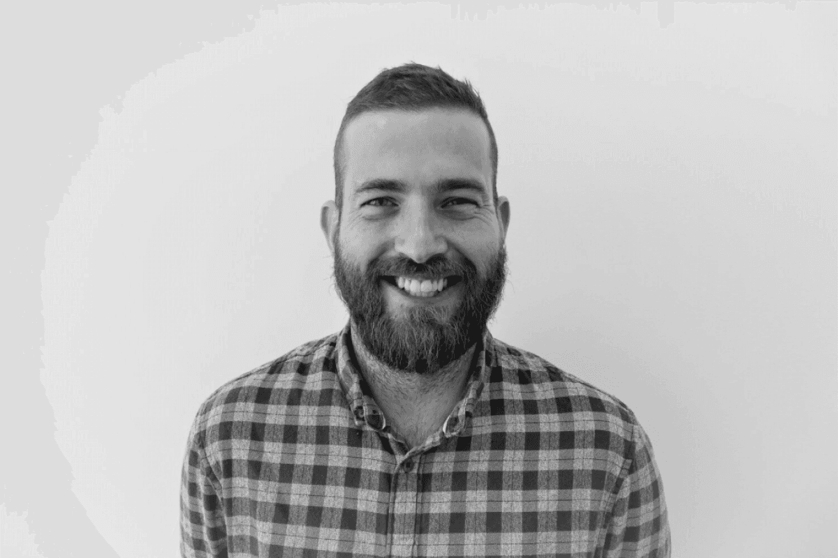 Jason smiling and wearing a check shirt standing in front of a white wall