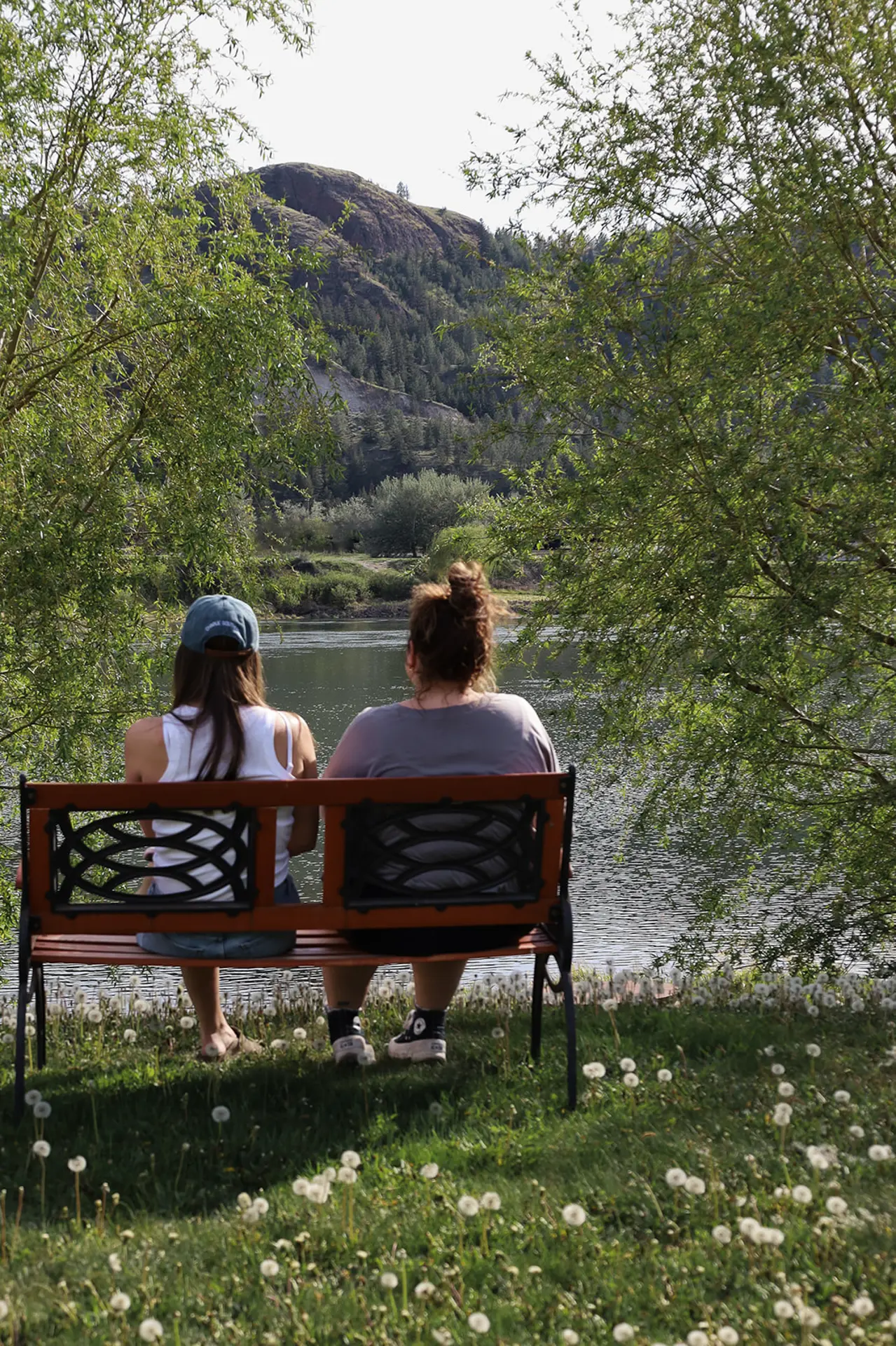 Two women sitting on a bench overlooking a lake with a mountain in the background.