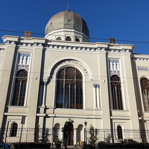 一座大型、華麗的建築,擁有圓頂、拱形窗戶和裝飾性元素。建築前有圍欄,上方是一片晴藍的天空。