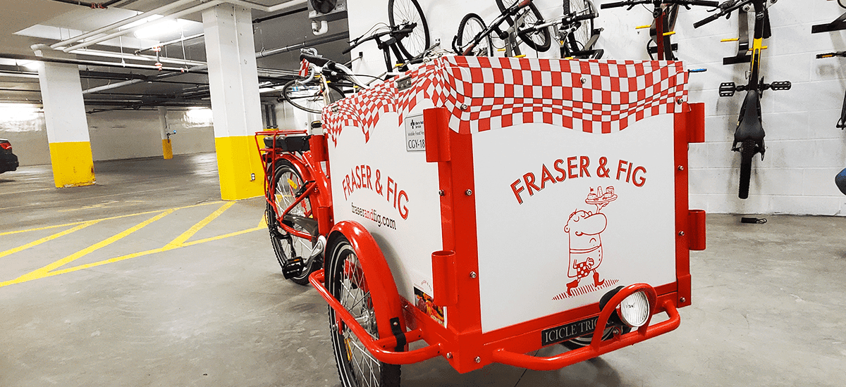 a red-and-white bicycle with fridge box attachment and vinyl wrap on top, reading Fig & Fraser on the sides and front