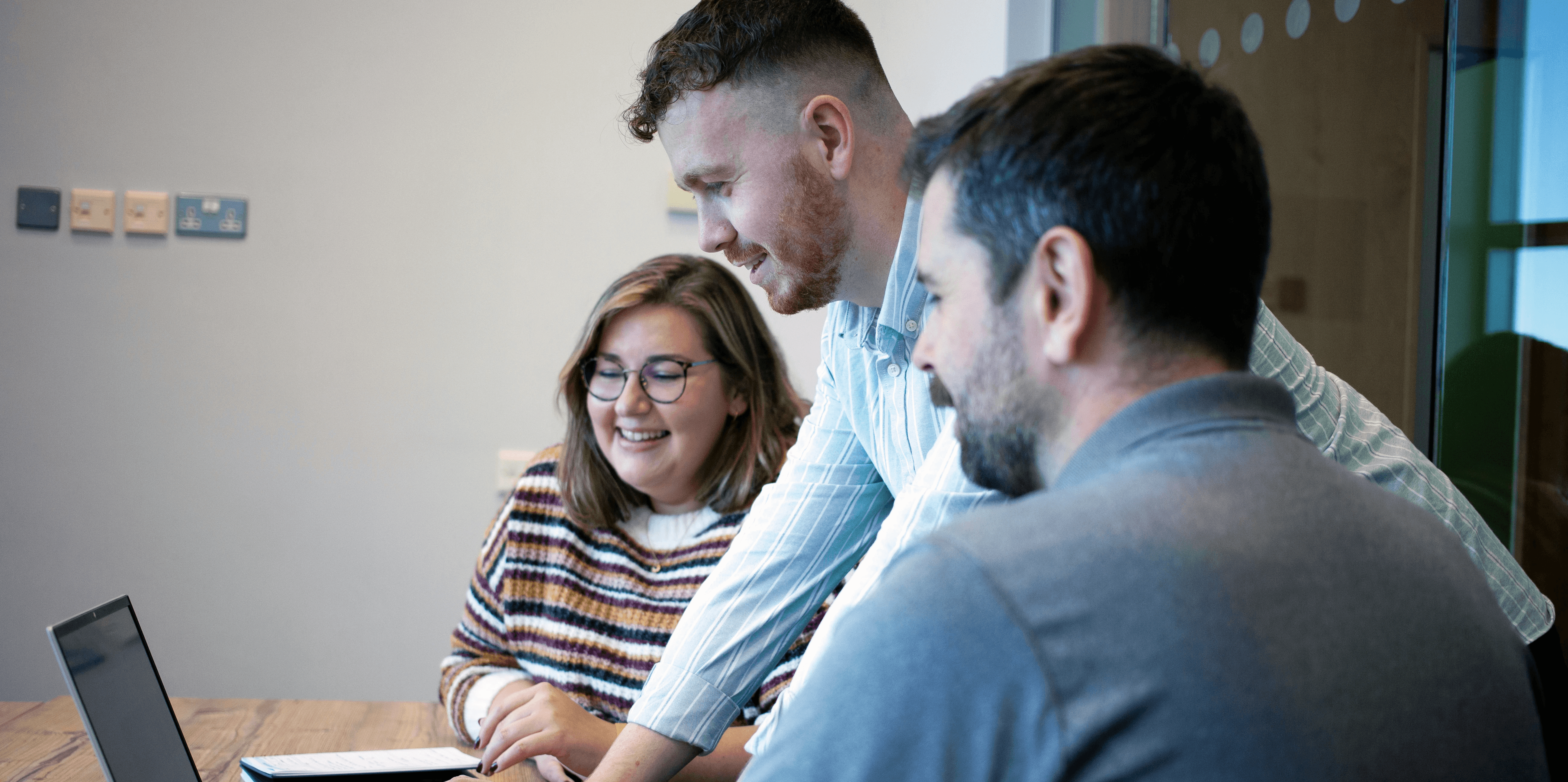 three staff members sat around a laptop, looking at the screen.
