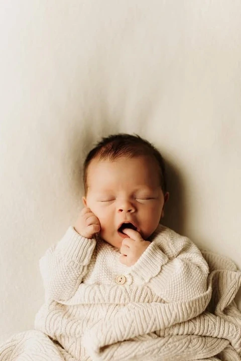Yawning newborn wrapped in a cream blanket