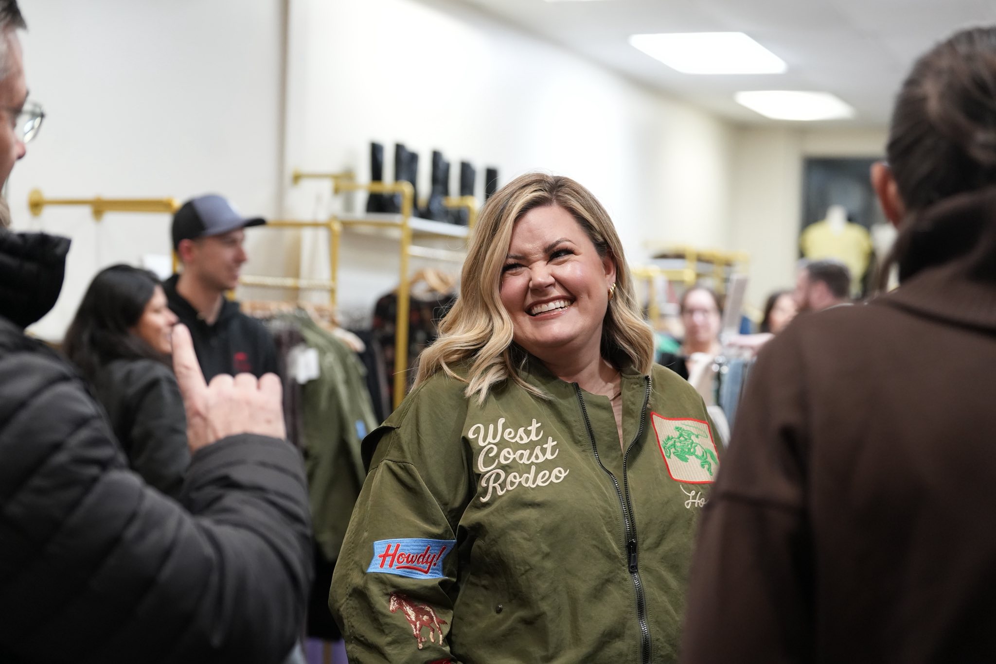 A person with long hair stands against a bright, hazy background, reaching out with one hand.
