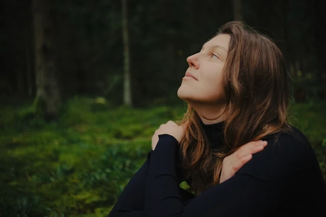 Woman outdoors in a forest with her head tilted upward