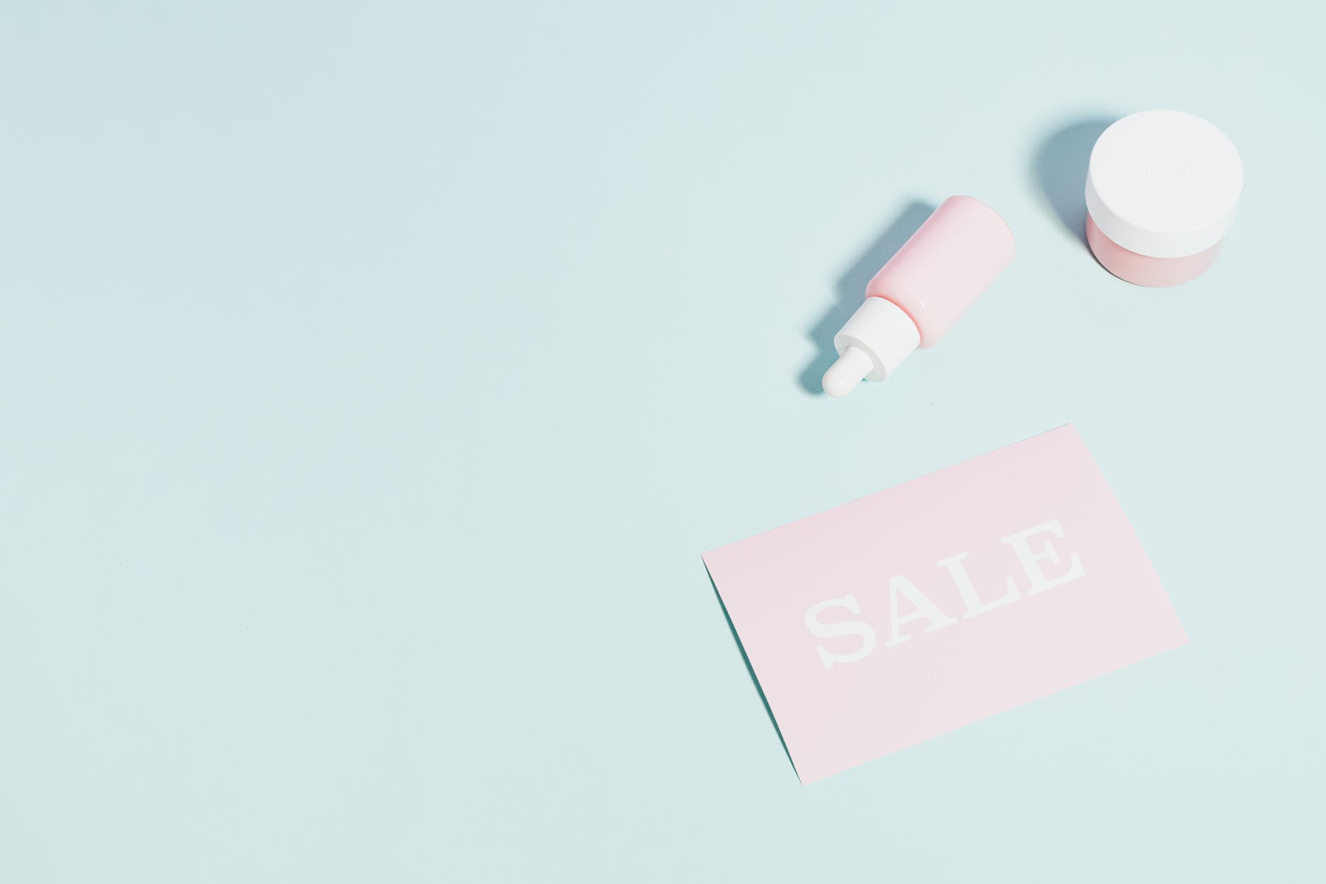 Pink beauty products and sale sign on pastel backdrop.