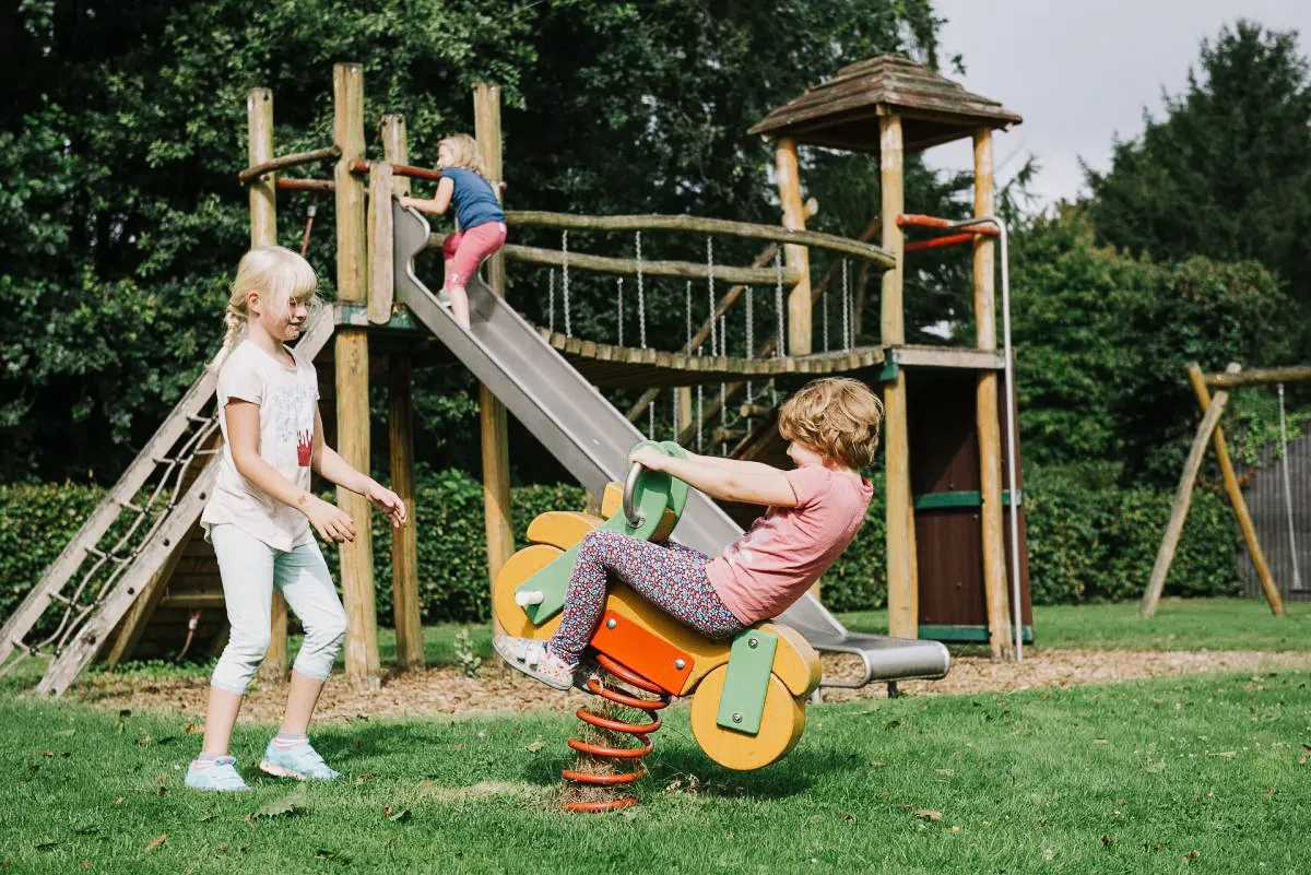Drei spielende Kinder auf einem Spielplatz mit Rutsche, Wippe und Klettergerüst. Fröhliche Kinder beim Spielen im Freien.