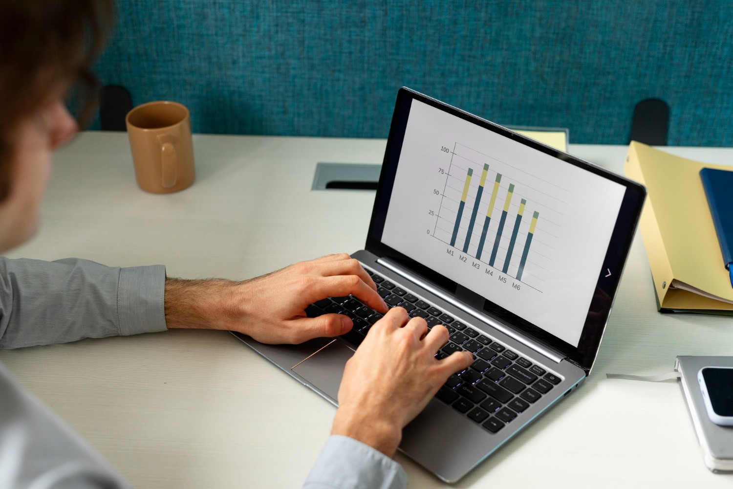 A man types on a laptop displaying a chart, focused on his work in a professional setting.