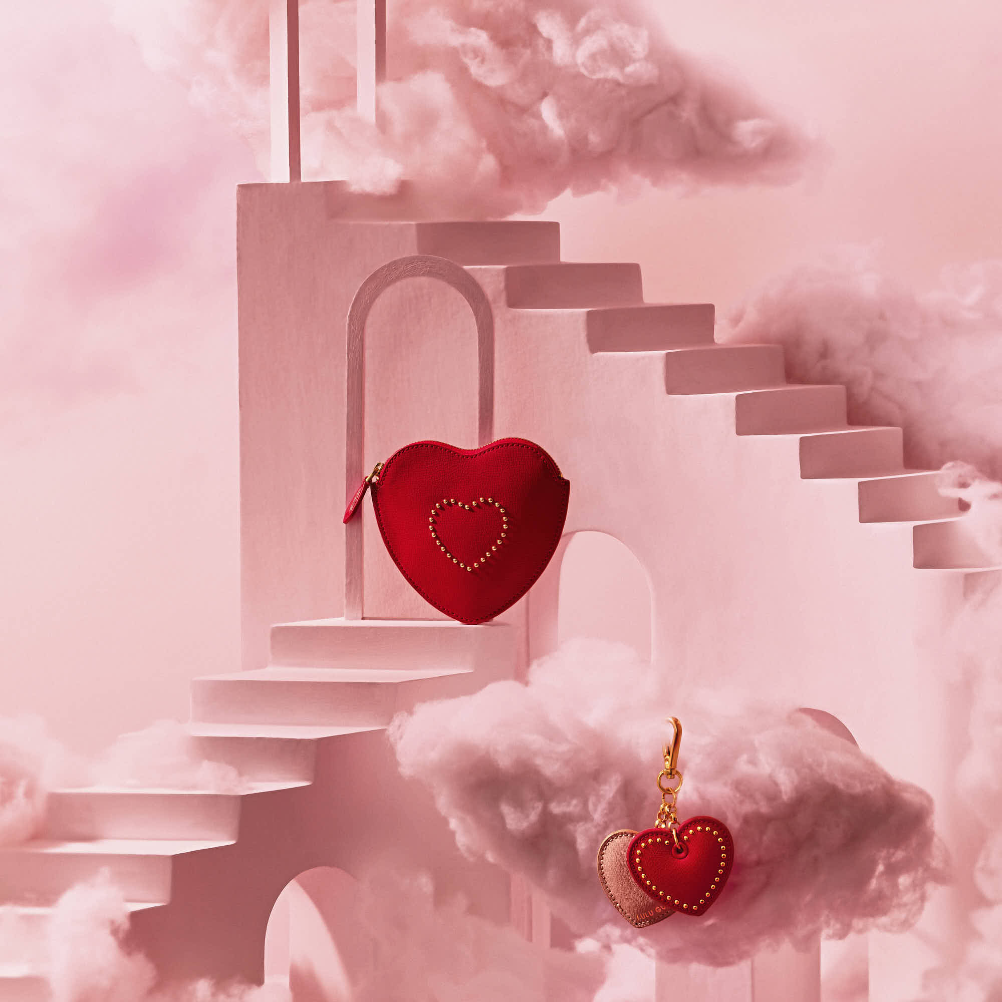 Red heart-shaped accessories with gold detailing on pink cloud and staircase backdrop.