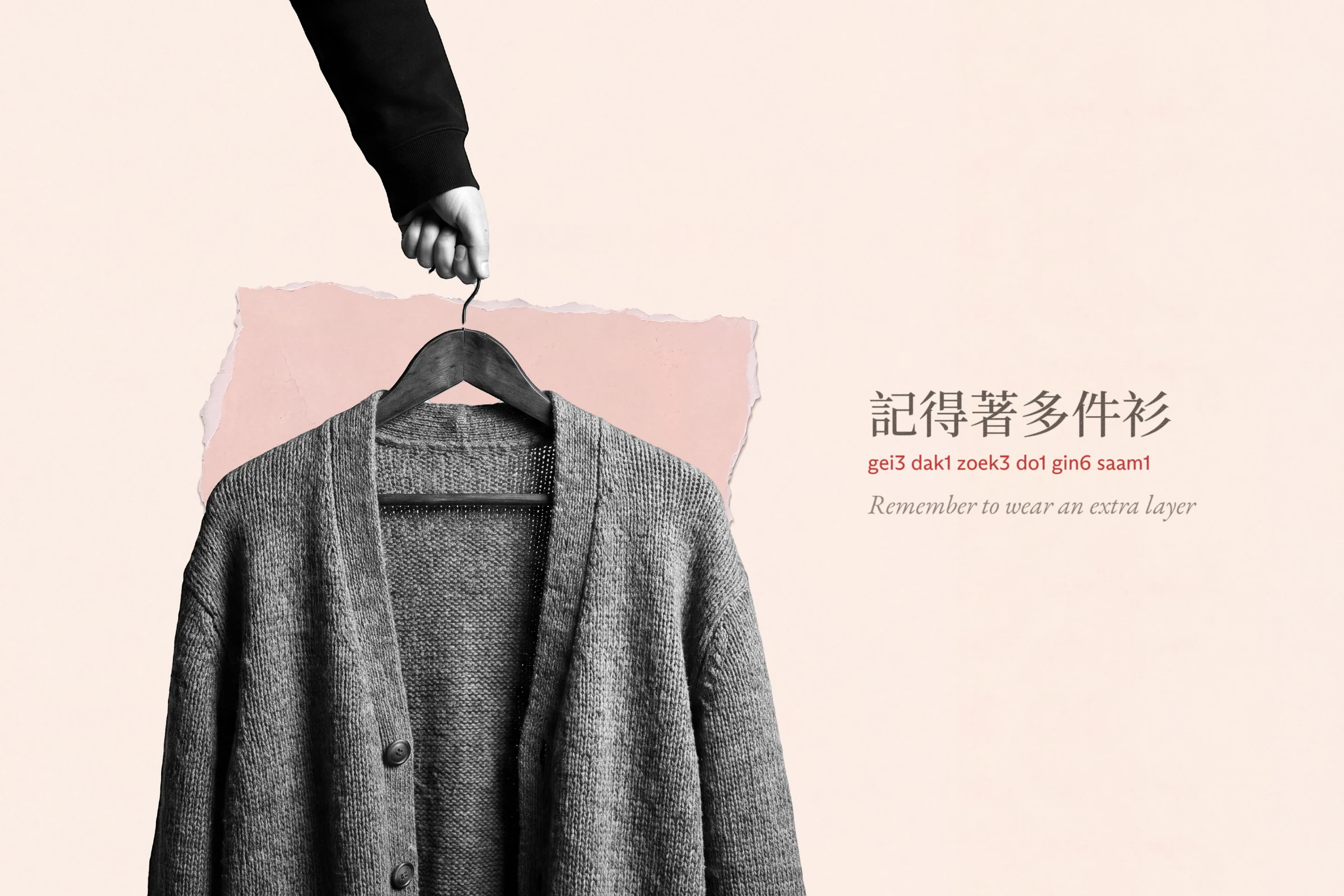 On cream paper with a torn blush patch, a black-and-white cut-out of a hand reaching down to hold up a knitted cardigan on a wooden hanger. Label: 記得著多件衫, gei3 dak1 zoek3 do1 gin6 saam1, remember to wear an extra layer.