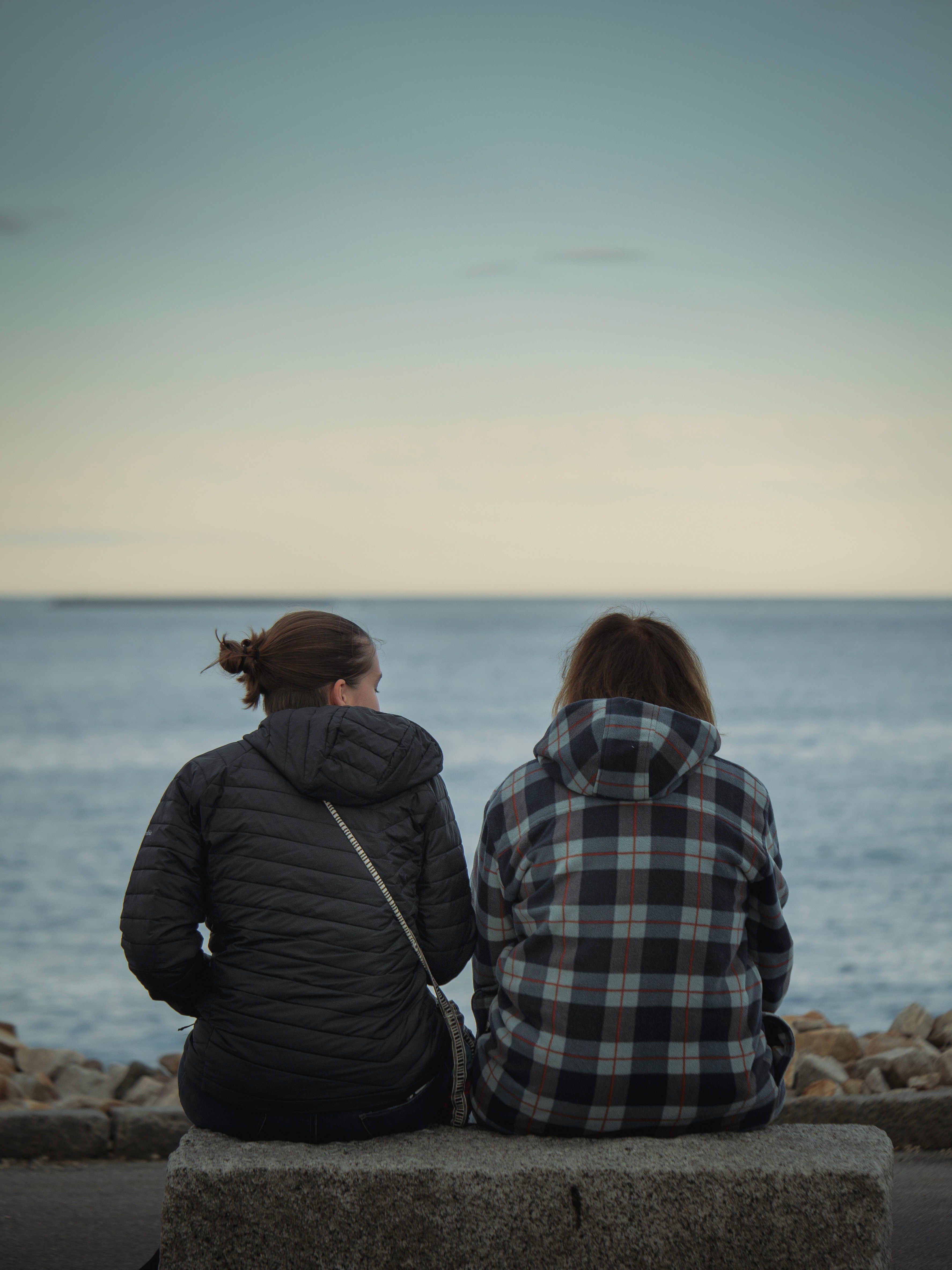two people sitting on a bench looking out at the ocean