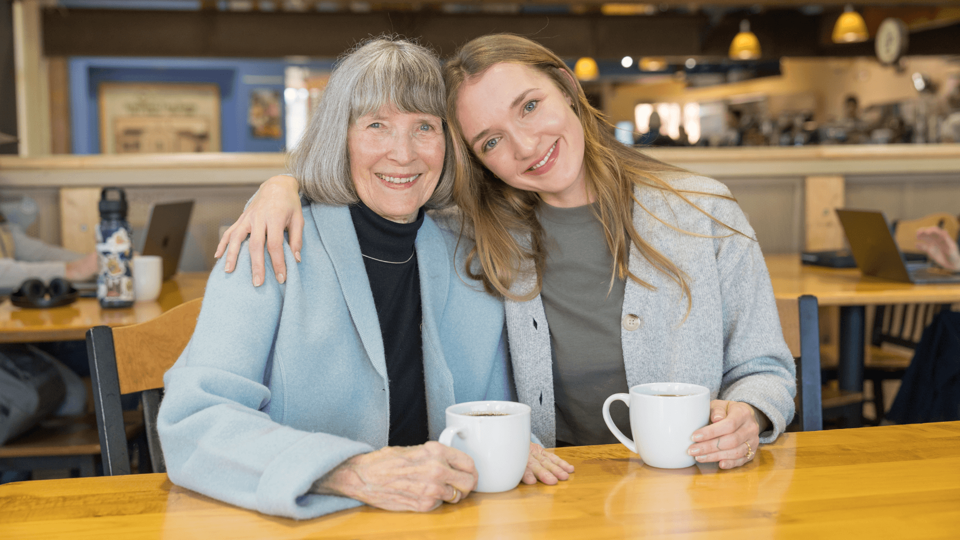 A person sitting at a bar counter, smiling, holding a drink, with a warm, inviting interior in the background.
