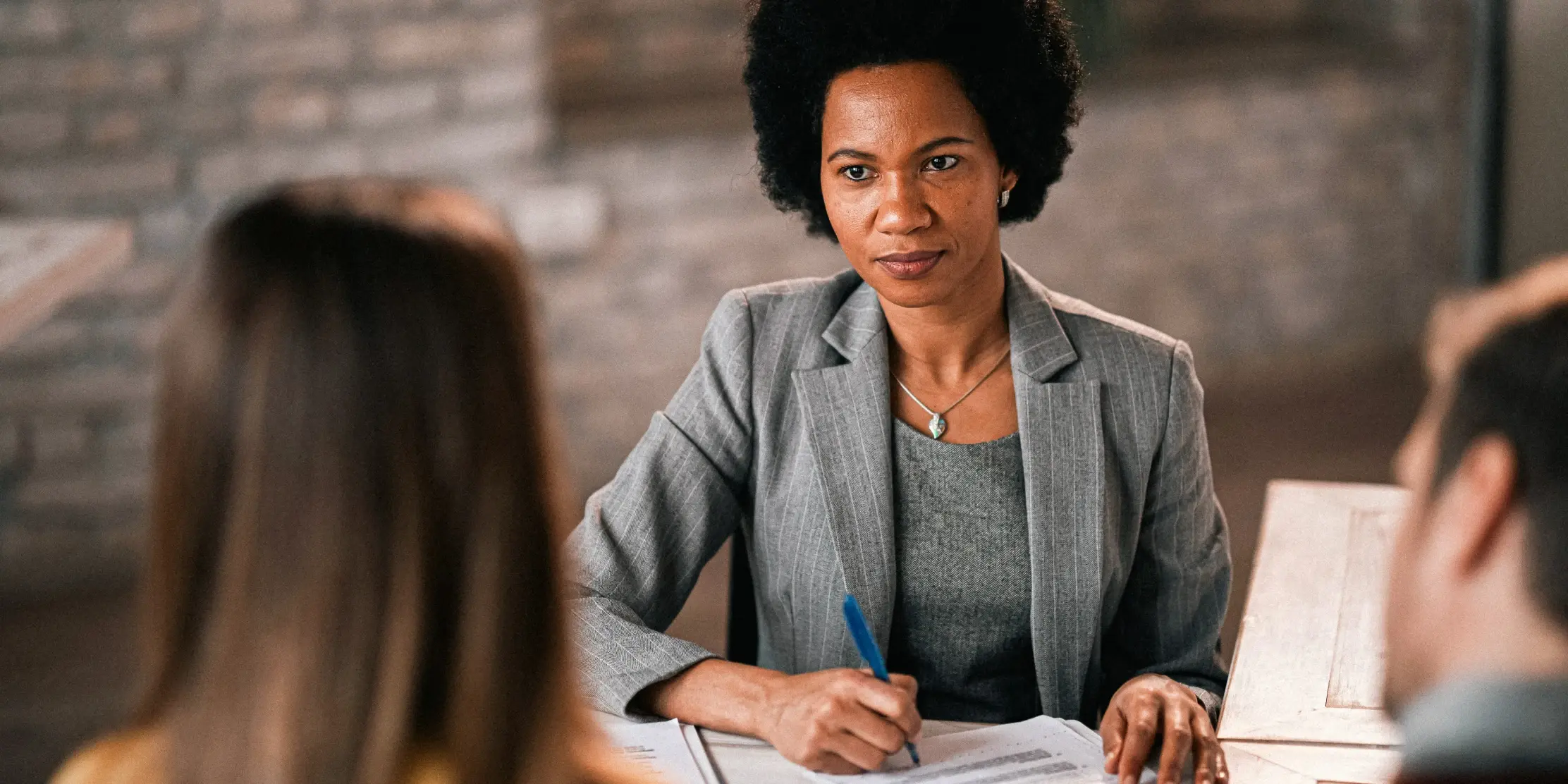 Professional woman in a gray pinstriped blazer and necklace reviewing documents during a meeting