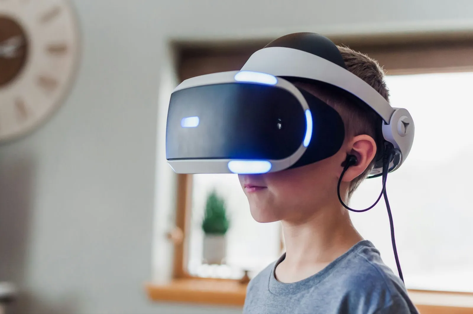 A young boy wearing a virtual reality headset with earphones, standing in a bright indoor setting.