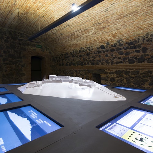 Isang silid na may mga pader na gawa sa ladrilyo at bato tampok ang 3D model display sa gitna na napapalibutan ng maraming interactive na screen.