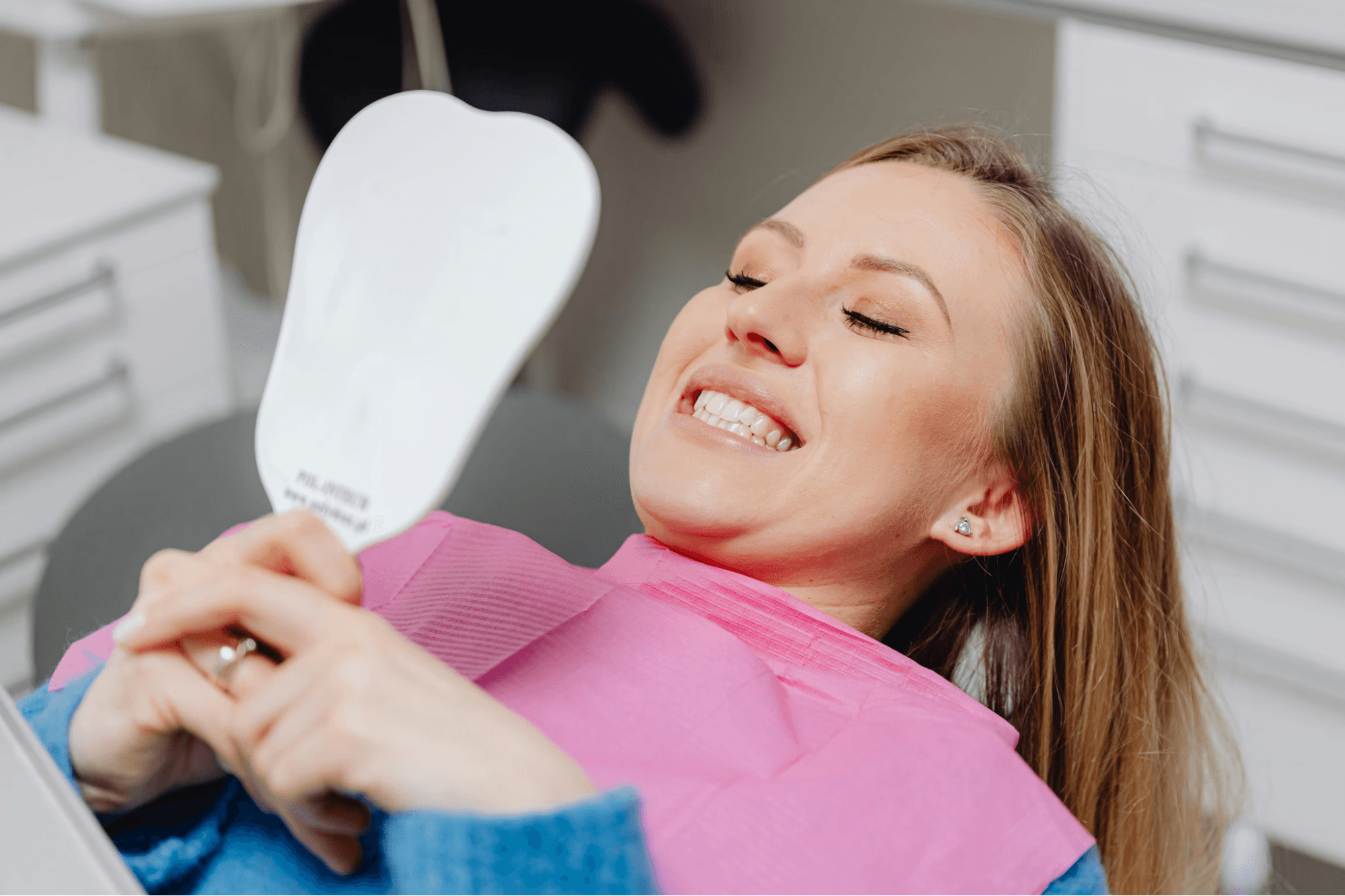 After gum pigmentation treatment, a woman looks at the mirror, highlighting her newly brightened gums and more balanced smile.
